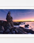 A coastal rock formation at sunset, from the Mana Island print, displayed in a white frame with a white mat.